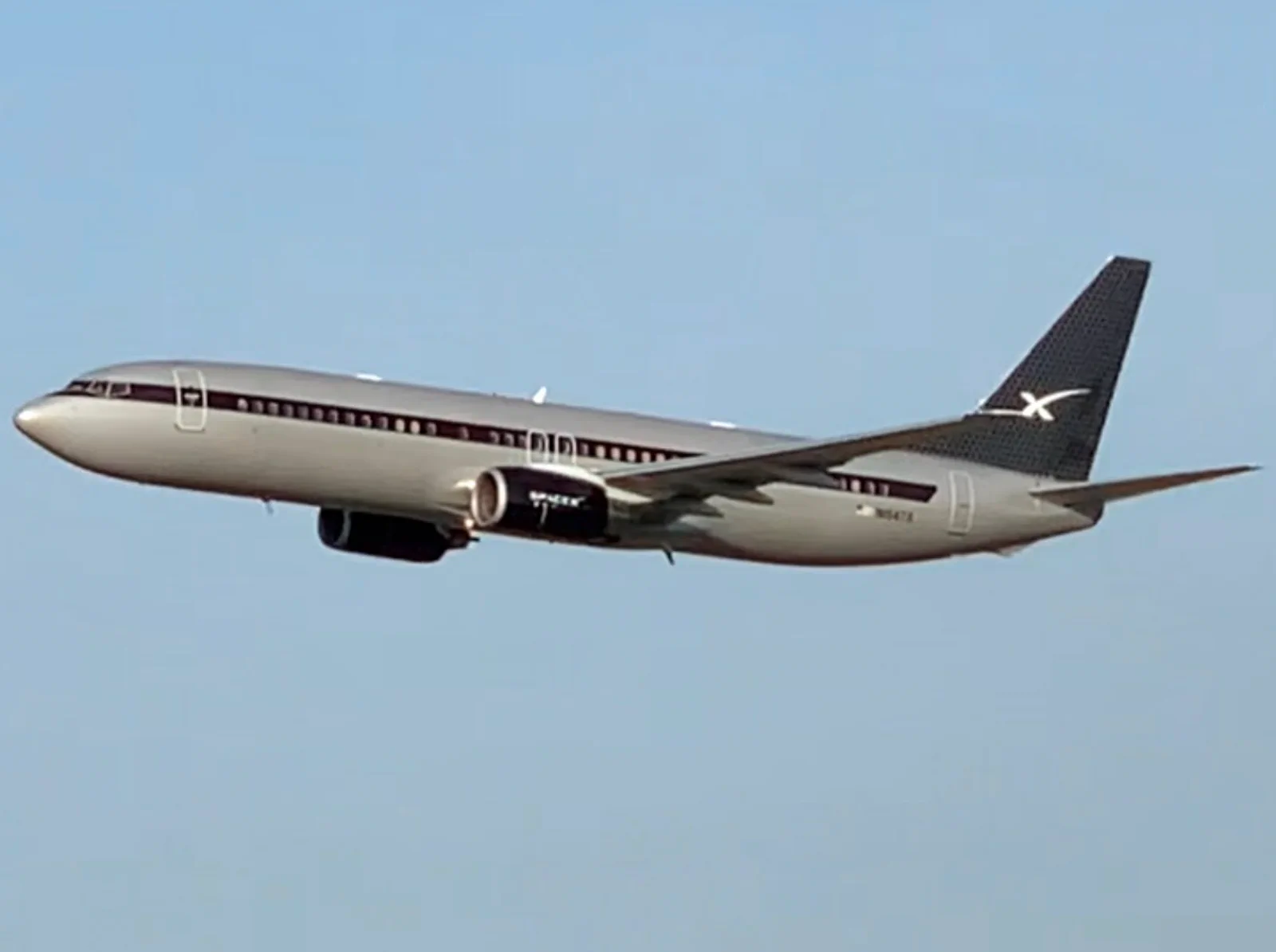 A silver executive Boeing 737 with a black SpaceX tail climbing out after takeoff