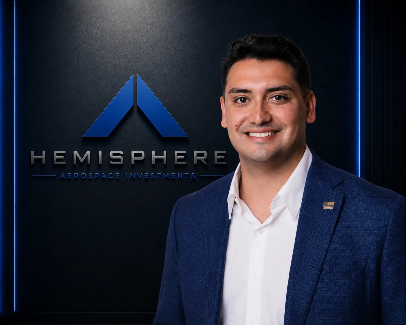 Tyler Sawyer in a blue jacket and open-collar white shirt, photographed beside the illuminated Hemisphere Aerospace Investments logo wall